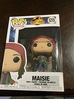 Front view of Funko Pop Jurassic World Maisie vinyl figure in original packaging, showing the character's name, series number 1215, and branding.