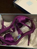 Pair of purple satin high heel sandals with ankle straps and rhinestone decoration, displayed inside shoebox with tissue paper.