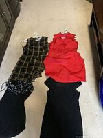 Four women's dresses laid flat on carpet floor, visible details include colors, neckline styles, and fabric patterns.