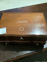 Closed wooden jewelry box showing curved edge design with metal handles on drawers.