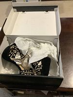 Pair of Justfab Tucson black shoes with tan cutout pattern in white box with tissue paper, size 8, approximately 5-inch heel.