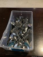 Plastic container filled with various pieces of kitchen cutlery including forks, spoons, and knives.