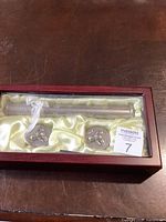 Front view of mahogany wood box with satin lining showing the rattle and two small containers inside.