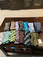 All 13 men's ties rolled and secured with rubber bands, displayed on a wooden table, showing various patterns and colors.