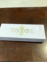 Closed TYME branded box on a wooden surface, white with gold logo and text.