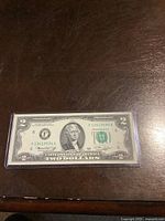 Front side of the 1976 Series $2 note featuring Thomas Jefferson, encased in a protective plastic holder on a wooden surface.