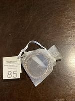 Photo showing one Swarovski crystal bracket in a white organza bag with the Maxsold auction label number 85 next to it on a dark wooden surface.