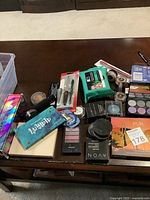 Photo showing various women's beauty products including nail files, makeup palettes, powders, brushes, and wipes on a table.