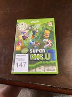 Photo of the closed green case showing the front cover art for New Super Luigi Bros U for Wii U with a MaxSold auction sticker.
