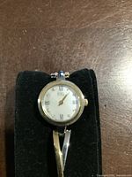 Front view of the ESQ by Movado women's wristwatch on a black cushion showing round white dial with roman numerals and gold tone bezel and bracelet.