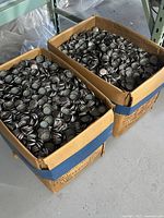Two large cardboard boxes filled to the top with unused metal Coca-Cola bottle caps.