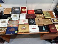 View of all 25 cigar boxes spread out on a large wooden desk showing various brands and colors