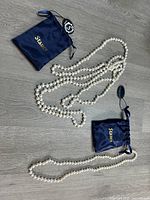 Two new cultured pearl necklaces laid out with their respective blue Stauer brand pouches on a wood surface.