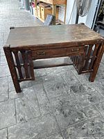 Front angle view showing the desk's main structure, drawer, and leg design on a tiled floor.