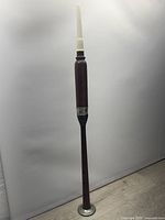 Full length image of the bagpipe trainer pipe showing the white mouthpiece and rosewood body with finger holes and metal ring near the base.