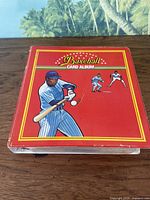 Photo of closed red baseball card album with baseball player illustrations on cover
