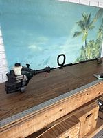 Full side view of the Bolens weed eater showing the engine, fuel tank, shaft, and handle on a wooden surface against a wall with tropical wallpaper.