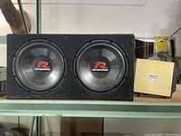 Renegade dual subwoofer speaker box and Phoenix Gold SX 2400.2 amplifier on a shelf, showing general wear and condition.