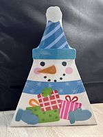 Photo of wooden snowman shaped advent calendar showing full front view with blue striped hat, carrot nose, coal eyes and mouth, and presents at the bottom.