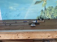 Three fishing rods with reels laid on table showing overall lot