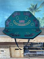 Full view of the octagonal fold away casino table topper resting on a wooden surface, showing eight player positions with cup and card holders and carry handles.
