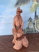 Full view of the wooden sculpture of a man holding a sack of coffee beans against a tropical background