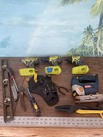 Overview of the lot including three yellow Ryobi cordless drill/drivers with batteries, Ryobi jigsaw, various hand tools and black tool belt.