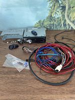 Photo showing JVC KD-S29 car CD receiver with wiring harness, mounting brackets, and plastic installation parts laid out on a wood surface with a background of palm trees.