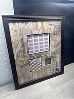 Full view of framed military memorial postal art showing uncut sheet of stamps, first day issue cover, and commemorative coin with patriotic artwork in background.