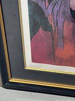 Close-up image showing the artwork's lower-left corner with part of the black and gold-trimmed frame and portion of the colored print.