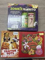 Photo showing three sealed board games: Zombie Burrito with box damage, Traitor Tots, and Yutnori.