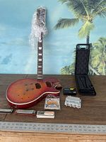 Wide shot of the lot showing vintage Harmony guitar body and neck, pickup cavities, bridge and tailpiece, harmonica case, amplifier, and packs of strings and other parts arranged on table