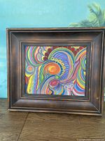 Frontal view of the framed colorful modern abstract painting with visible wooden frame.