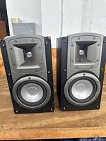 Front view of the pair of Klipsch Synergy B2 bookshelf speakers showing the horn tweeters and silver woofers in black cabinets on wooden surface.