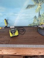 Photo of weedwhacker tool laid down with battery charger and battery on table, Ryobi branding visible.