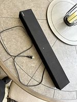 Samsung black sound bar on beige tiled surface with power cord visible.