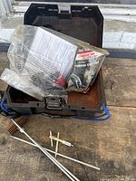 Top-down image of open Dewalt toolbox showing tubing cutter in sealed plastic packaging laid inside, with three cleaning rods arranged on the table in front.