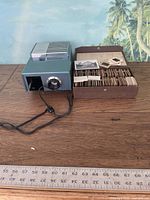 Vintage Argus special slide projector with attached power cord, shown on wooden surface with vintage slide case.