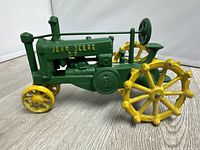 Front-left angled view of the green and yellow cast iron John Deere tractor toy showing detailed wheels, engine block, and steering wheel.