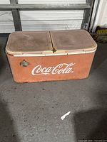 Side view of vintage Coca Cola cooler showing faded hinged lids and Coca Cola logo on front