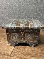 Front view of the rectangular jewelry box showing copper and silver colored metal with floral tooling and elephant motifs on panels and feet.