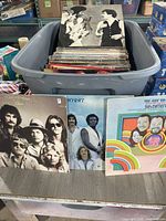 Plastic tote filled with multiple vintage LP records. Three LP covers displayed in front include Firefall's 'Elan', Three Dog Night, and The 5th Dimension.
