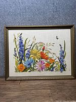 Full view of vintage needlepoint floral artwork framed with a wooden frame, showing colorful flowers and a bee in the top right area.
