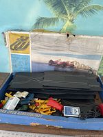 Box and track pieces inside with slot cars and controller visible