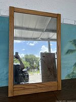 Front view of the vintage wall mirror with medium-toned wood frame reflecting an outdoor scene and ceiling.