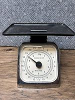 Front facing photo of vintage Salter mechanical scale showing white dial with black numbers and needle, black weighing tray on top, chrome body reflecting surroundings.