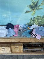 Wide shot showing array of folded women's clothing items in various colors and styles laid out on a table with tropical backdrop.