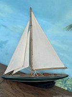 Full side view of the wooden model sailboat showing tall white sails, dark green and black hull, and wooden deck detail.