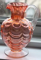 Front view of cranberry glass pitcher showing scalloped body and clear handle