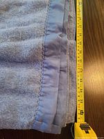Folded blue electric blanket with tape measure showing width, satin edge visible